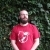 Un homme barbu avec des lunettes et une forte calvitie porte un t-shirt rouge du drupalcamp lannion 2017, son expression est neutre, il regarde au loin